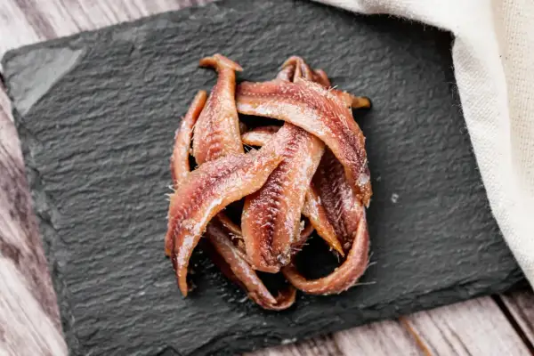 Kupa rybek anchois ułożona na czarnej desce, gotowa do podania.