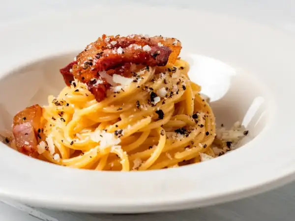 Pyszne spaghetti all'amatriciana z chrupiącym guanciale i startym parmezanem, posypane świeżo mielonym pieprzem.