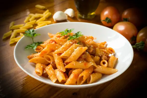 Penne rigate w sosie pomidorowym z parmezanem, ozdobione natką pietruszki. To klasyczne danie, które pokazuje, co to jest penne.