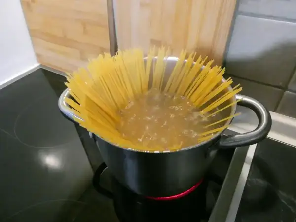 Długie spaghettoni gotują się w garnku na kuchence.