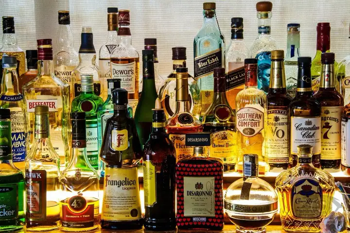 Różnorodne rodzaje alkoholi: whisky, likiery, gin, brandy i inne, stojące na półce.
